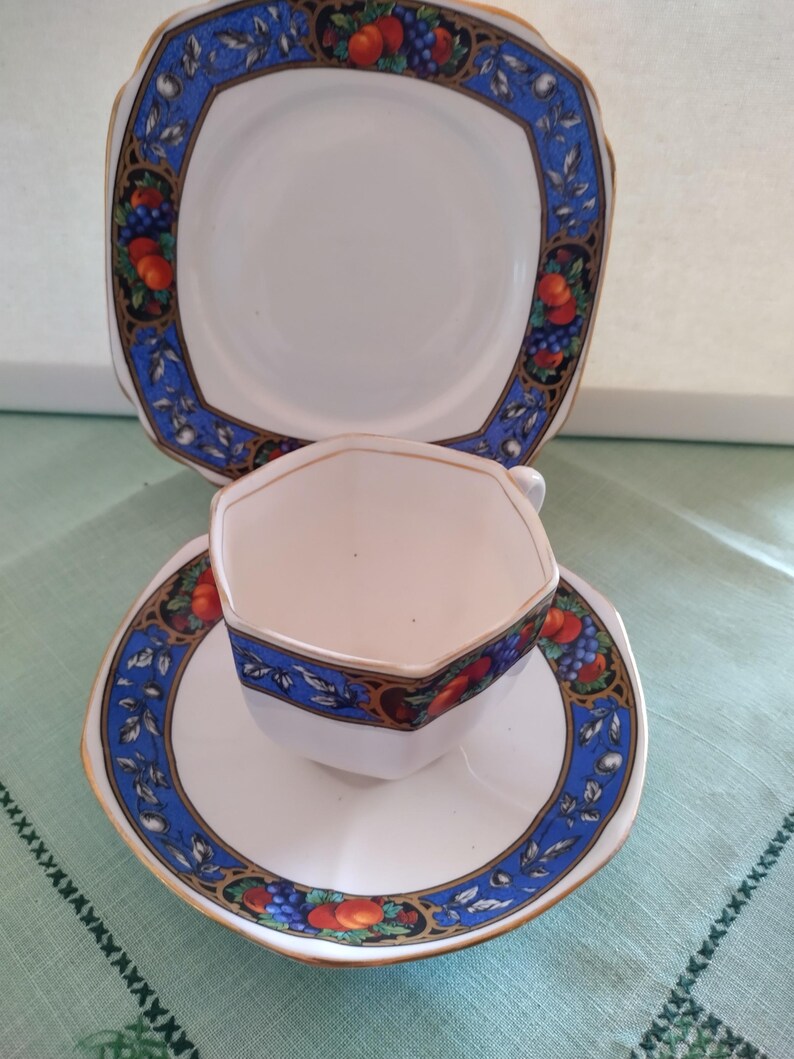 Puede incluir: Un juego de taza y platillo de t&eacute; blanco con un patr&oacute;n floral azul y dorado. La taza y el platillo tienen forma hexagonal.