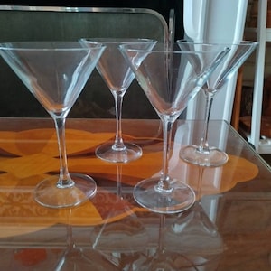 May include: Four clear glass martini glasses on a wooden table with a glass top. The glasses are empty and are arranged in a row.