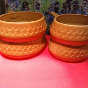 May include: Two brown ceramic bowls with a diamond pattern stacked on top of each other. The bowls have a handle on one side.