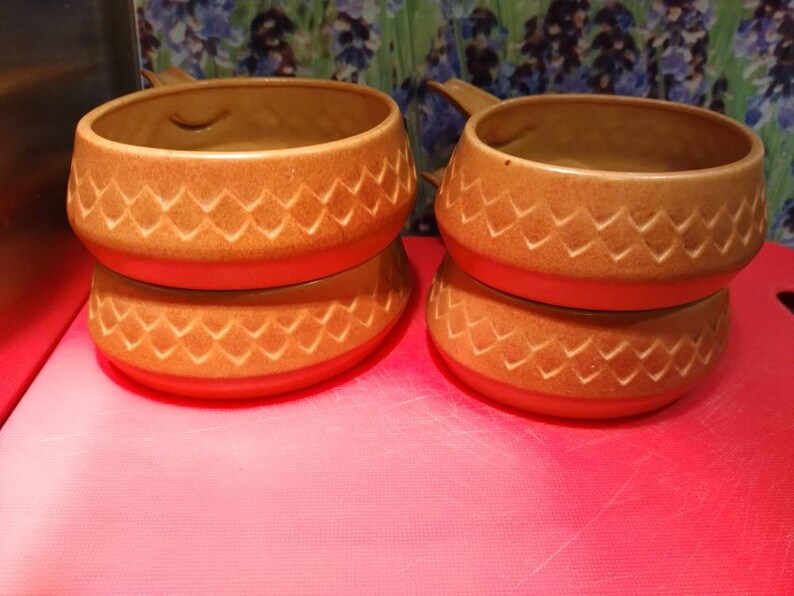 May include: Two brown ceramic bowls with a diamond pattern stacked on top of each other. The bowls have a handle on one side.