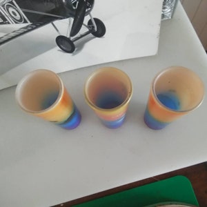 May include: Three colorful glass shot glasses with a rainbow design. The glasses are clear with a blue, yellow, orange, and red gradient.