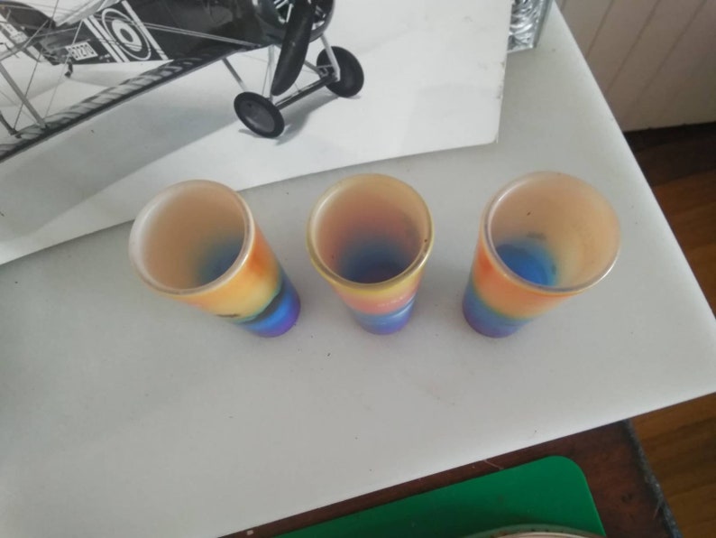 May include: Three colorful glass shot glasses with a rainbow design. The glasses are clear with a blue, yellow, orange, and red gradient.