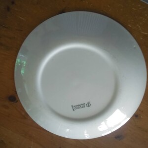 K&ouml;nnte beinhalten: Ein wei&szlig;er Keramikteller mit einem erh&ouml;hten Rand und einer dezenten strukturierten Oberfl&auml;che. Der Teller hat ein kleines Logo in der Mitte, das "Studio Nova" lautet.