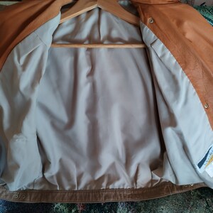 Puede incluir: Una chaqueta de cuero marr&oacute;n con un forro de color marr&oacute;n claro. La chaqueta tiene una cremallera y un cuello abotonado. El forro tiene una etiqueta que dice "Leather World".