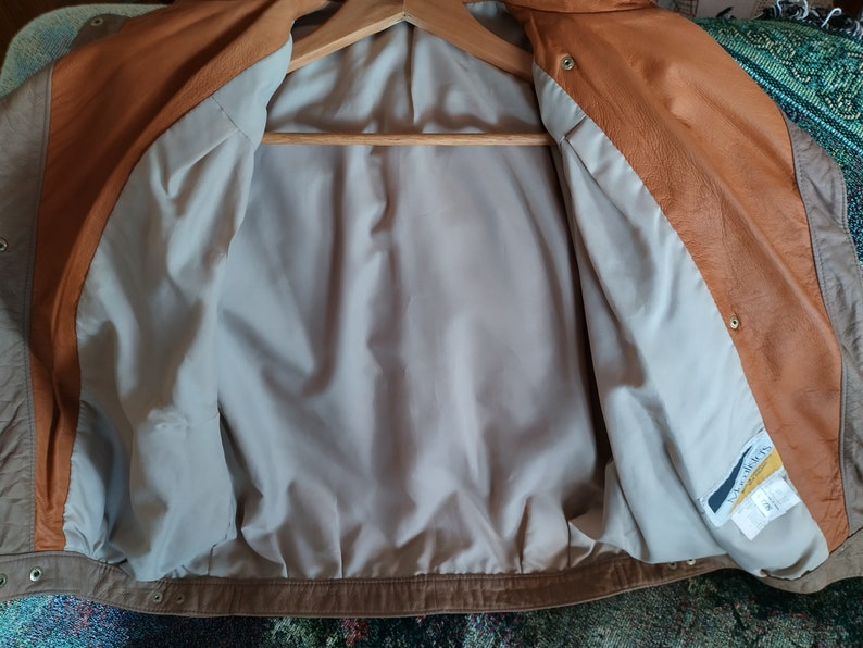 Puede incluir: Una chaqueta de cuero marr&oacute;n con un forro de color marr&oacute;n claro. La chaqueta tiene una cremallera y un cuello abotonado. El forro tiene una etiqueta que dice "Leather World".