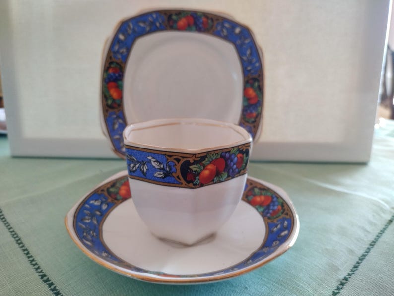 Puede incluir: Un juego de taza y platillo de t&eacute; blanco con un patr&oacute;n floral azul y dorado. La taza tiene una forma hexagonal y el platillo tiene un borde festoneado.