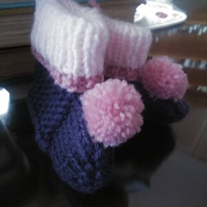 May include: A pair of knitted baby booties with pink pom-poms. The booties are purple and white with a pink stripe.