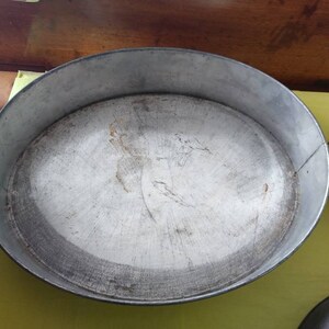 K&ouml;nnte beinhalten: Eine ovale Backform aus Metall mit silbernem Finish, die Gebrauchsspuren aufweist. Die Form hat einen erh&ouml;hten Rand und eine abgenutzte Innenseite. Eine runde Backform ist ebenfalls im Bild zu sehen.