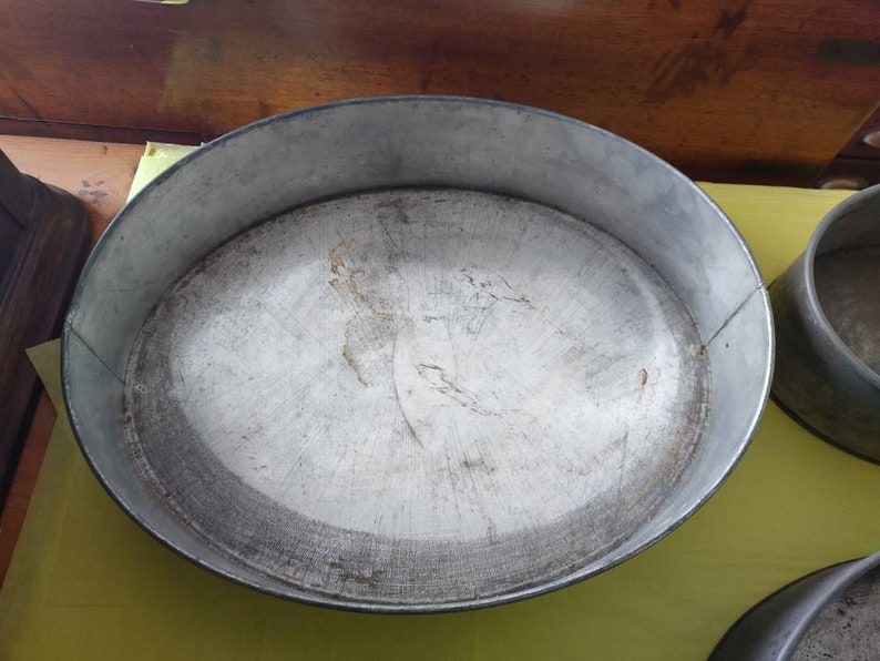 K&ouml;nnte beinhalten: Eine ovale Backform aus Metall mit silbernem Finish, die Gebrauchsspuren aufweist. Die Form hat einen erh&ouml;hten Rand und eine abgenutzte Innenseite. Eine runde Backform ist ebenfalls im Bild zu sehen.