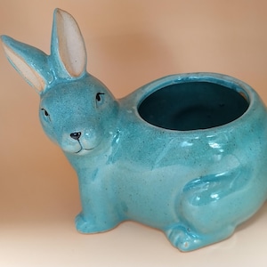 May include: A turquoise ceramic planter shaped like a rabbit. The planter has a glazed finish and a small opening at the top for planting.