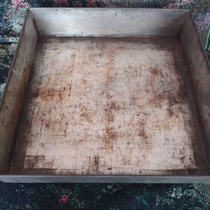 May include: A silver baking sheet with a worn, scratched surface. The sheet is rectangular and has a raised rim.