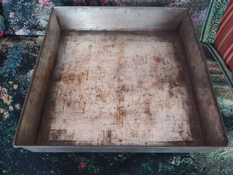 May include: A silver baking sheet with a worn, scratched surface. The sheet is rectangular and has a raised rim.