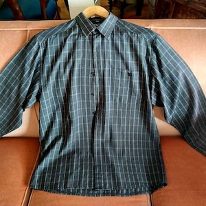 May include: A long-sleeved, button-down shirt with a black and white checked pattern. The shirt has a single chest pocket.