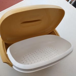 May include: A yellow-beige plastic food container with a white, perforated insert. The lid is open, showing the inside. The container is designed for food storage and transport, ideal for picnics.