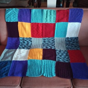 May include: A knitted patchwork blanket with squares in various colours, including blue, red, yellow, and green.