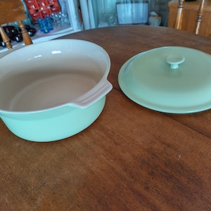May include: A light green ceramic casserole dish with a matching lid. The dish has a white interior and a round shape. The lid has a knob on top.