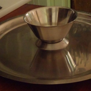 May include: A silver serving tray with a decorative design on the handles and a small, round, silver bowl in the center.