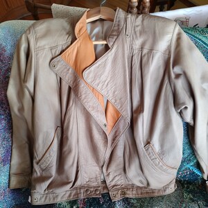 Puede incluir: Una chaqueta de cuero marr&oacute;n con forro beige. La chaqueta tiene cierre de cremallera y dos bolsillos.