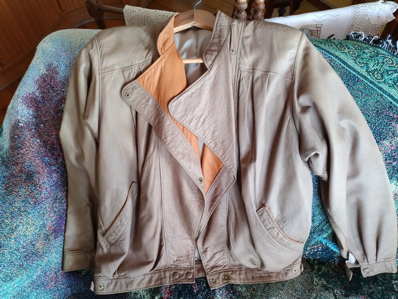 Puede incluir: Una chaqueta de cuero marr&oacute;n con forro beige. La chaqueta tiene cierre de cremallera y dos bolsillos.