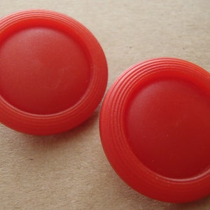 May include: Two bright red plastic buttons with a raised, circular design. The buttons have a smooth, glossy finish.