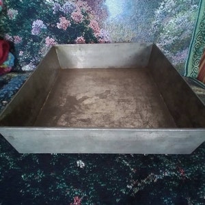 May include: A silver metal baking pan with a rectangular shape. The pan has a slightly worn surface.