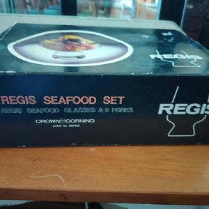 Puede incluir: Una caja negra con el texto "REGIS SEAFOOD SET 6 REGIS SEAFOOD GLASSES & 6 FORKS CROWN CORNING CODE No 160142 REGIS" impreso en ella. La caja contiene un juego de seis vasos para mariscos.