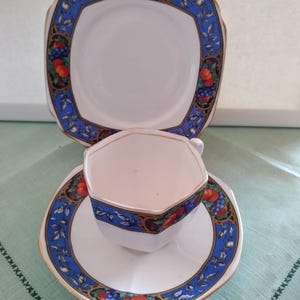 Puede incluir: Un juego de taza y platillo de t&eacute; blanco con un borde azul y dorado y un dise&ntilde;o de frutas. El platillo es de forma cuadrada y la taza es octogonal.