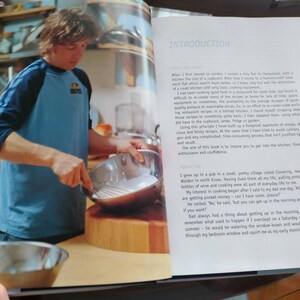 Puede incluir: Un hombre con una camiseta de b&eacute;isbol azul y negra est&aacute; cocinando en una cocina. Est&aacute; sosteniendo un batidor de metal y una sart&eacute;n de acero inoxidable. La cocina tiene una encimera de madera y una tabla de cortar de madera.