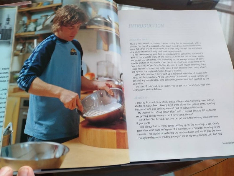 Puede incluir: Un hombre con una camiseta de b&eacute;isbol azul y negra est&aacute; cocinando en una cocina. Est&aacute; sosteniendo un batidor de metal y una sart&eacute;n de acero inoxidable. La cocina tiene una encimera de madera y una tabla de cortar de madera.