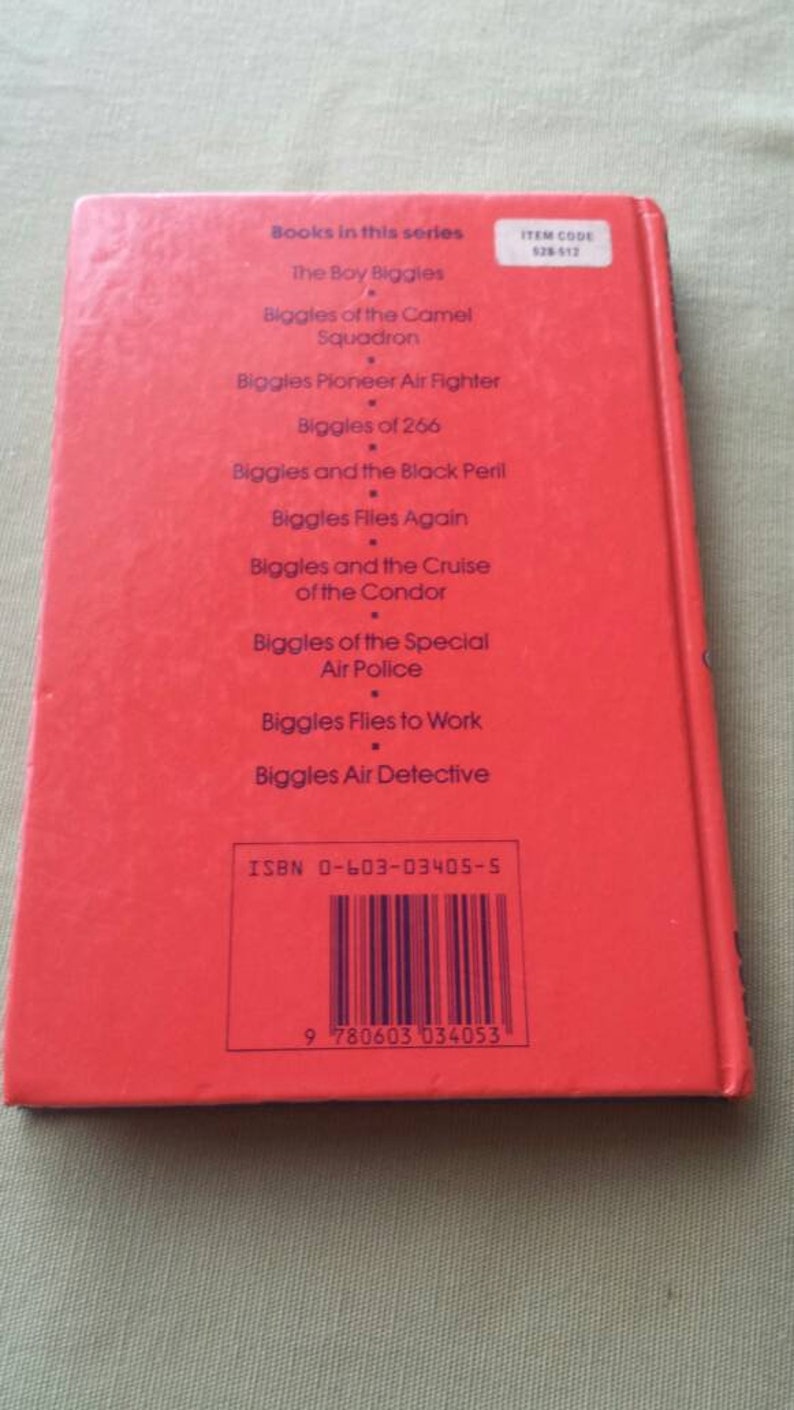 May include: A red book with a list of titles from the "Biggles" series. The titles include "The Boy Biggles", "Biggles of the Camel Squadron", and "Biggles Pioneer Air Fighter". The book has an ISBN and item code.