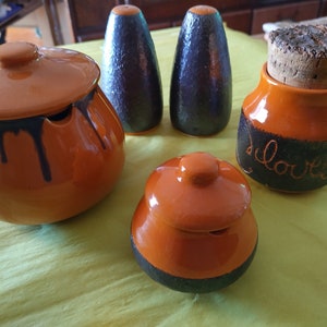 May include: Set of four brown and black ceramic kitchen canisters with lids. The canisters are labelled "cloves", "salt", "pepper", and "sugar".