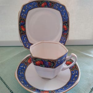 Puede incluir: Un juego de taza y platillo de t&eacute; vintage con un patr&oacute;n floral azul y dorado. La taza de t&eacute; tiene una forma hexagonal y el platillo tiene un borde festoneado.