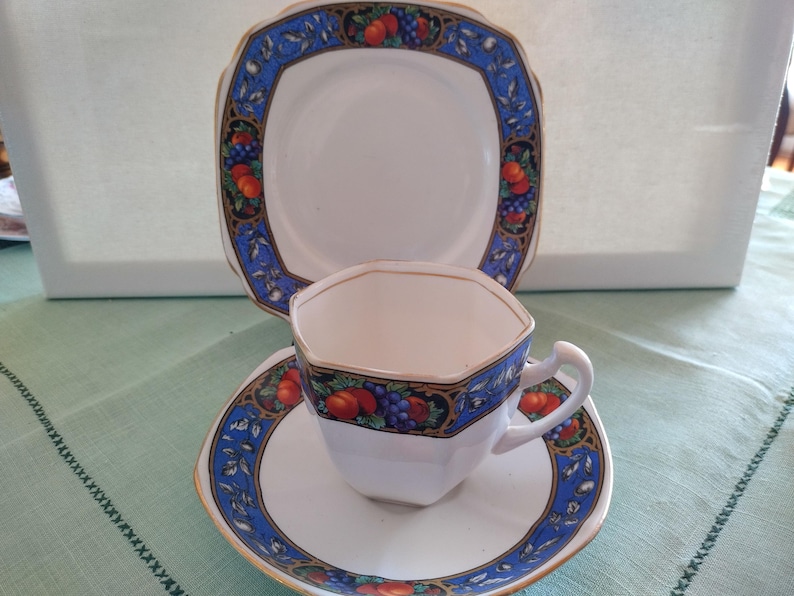 Puede incluir: Un juego de taza y platillo de t&eacute; vintage con un patr&oacute;n floral azul y dorado. La taza de t&eacute; tiene una forma hexagonal y el platillo tiene un borde festoneado.