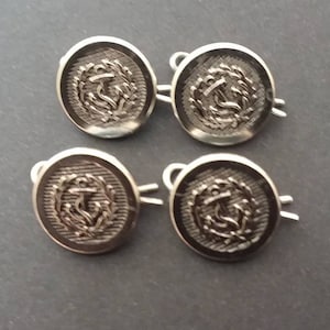 May include: Four silver-toned buttons with an anchor and wreath design. The buttons have a shank on the back for sewing.