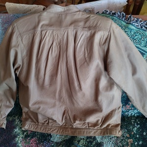 Puede incluir: Una chaqueta de cuero marr&oacute;n claro con cierre de cremallera y cuello abotonado. La chaqueta tiene una textura lisa y desgastada y una apariencia ligeramente arrugada.