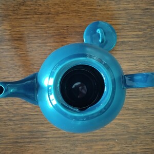 Puede incluir: Una tetera azul turquesa con una tapa a juego. La tetera tiene un cuerpo redondo y un pico en el lateral. La tapa tiene una peque&ntilde;a asa en la parte superior.