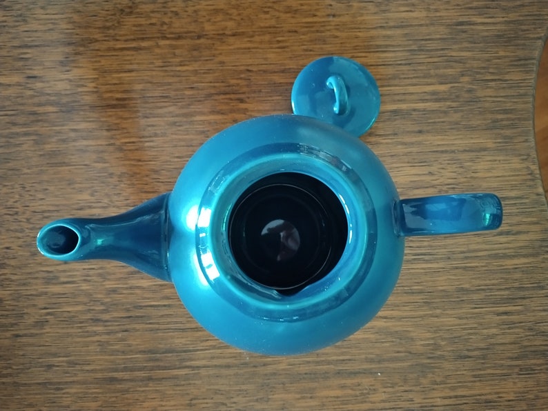 Puede incluir: Una tetera azul turquesa con una tapa a juego. La tetera tiene un cuerpo redondo y un pico en el lateral. La tapa tiene una peque&ntilde;a asa en la parte superior.