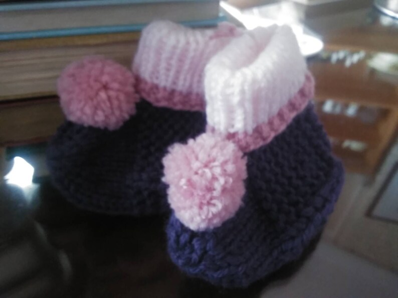May include: A pair of knitted baby booties with pink pom-poms and a purple and white striped cuff.