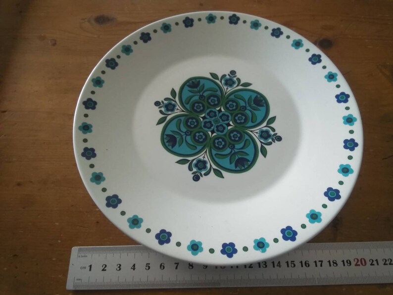 K&ouml;nnte beinhalten: Ein wei&szlig;er Keramik-Dinnerteller mit einem blauen und gr&uuml;nen Blumendesign. Der Teller hat einen blauen und gr&uuml;nen Rand mit kleinen wei&szlig;en Blumen.
