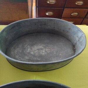 K&ouml;nnte beinhalten: Eine ovale Backform aus verzinktem Metall mit leicht abgenutztem Finish. Die Form hat einen abgerundeten Rand und einen flachen Boden. Die Form wird wahrscheinlich zum Backen oder Servieren von Speisen verwendet. Die Form steht auf einer gelben Oberfl&auml;che.