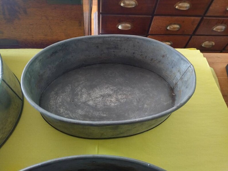 K&ouml;nnte beinhalten: Eine ovale Backform aus verzinktem Metall mit leicht abgenutztem Finish. Die Form hat einen abgerundeten Rand und einen flachen Boden. Die Form wird wahrscheinlich zum Backen oder Servieren von Speisen verwendet. Die Form steht auf einer gelben Oberfl&auml;che.