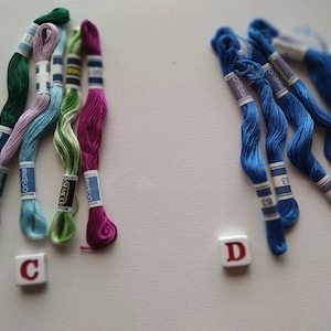 May include: Assortment of embroidery floss spools in various colours, including green, pink, blue, and purple. The spools are labelled with the brand name "Anchor" and the text "DMC Cotton".