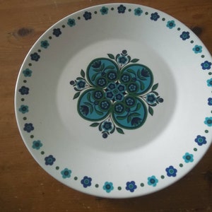 K&ouml;nnte beinhalten: Ein wei&szlig;er Keramikteller mit einem blauen und gr&uuml;nen Blumendesign. Der Teller hat einen gewellten Rand und ein blaues und gr&uuml;nes Blumendesign um den Rand.