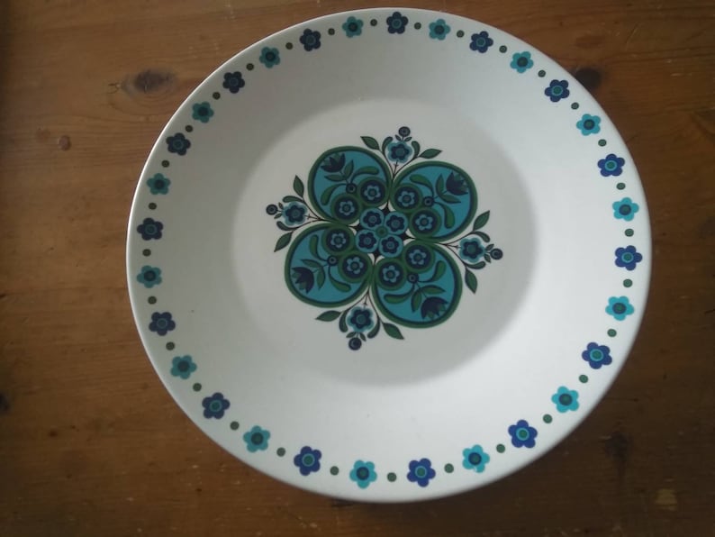 K&ouml;nnte beinhalten: Ein wei&szlig;er Keramikteller mit einem blauen und gr&uuml;nen Blumendesign. Der Teller hat einen gewellten Rand und ein blaues und gr&uuml;nes Blumendesign um den Rand.