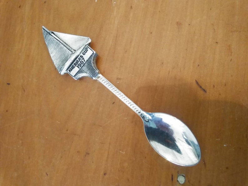 May include: Silver teaspoon with a sailboat design on the handle. The sailboat has the words "America's Cup 1987" on it.