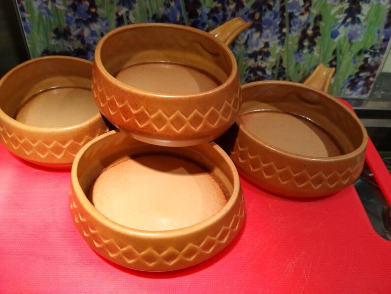 May include: Set of four brown ceramic bowls with handles. The bowls have a diamond pattern around the rim.