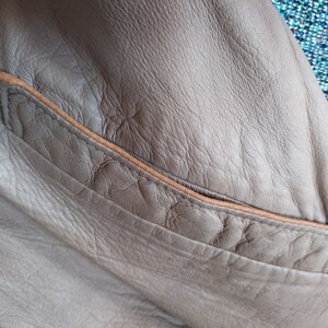 Puede incluir: Primer plano de una chaqueta de cuero marr&oacute;n con un bolsillo de cuero marr&oacute;n. El bolsillo tiene una costura marr&oacute;n cosida.