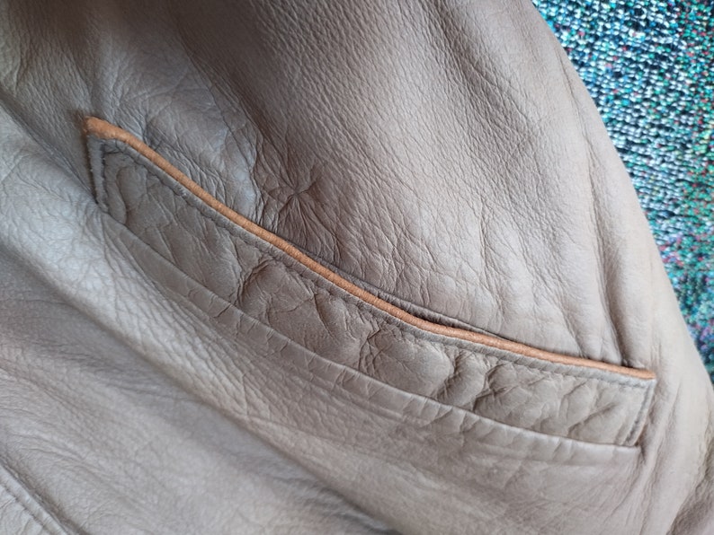 Puede incluir: Primer plano de una chaqueta de cuero marr&oacute;n con un bolsillo de cuero marr&oacute;n. El bolsillo tiene una costura marr&oacute;n cosida.