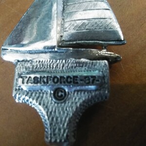 May include: A silver sailboat charm with the inscription "TASKFORCE-37-  &copy;" on the base.