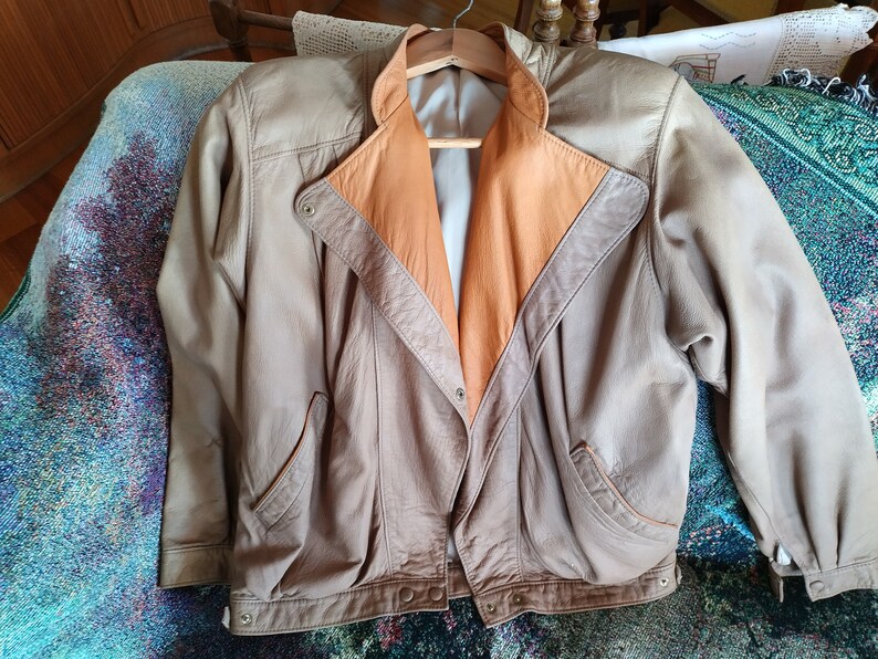 Puede incluir: Una chaqueta de cuero marr&oacute;n con forro de cuero beige. La chaqueta tiene cierre de cremallera y dos bolsillos.